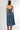 A woman wearing a strapless tiered denim maxi dress in a medium blue wash, paired with a brown baseball cap that reads 'Laguna BEACH' and layered gold necklaces-Fleastyle