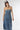 A woman wearing a strapless tiered denim maxi dress in a medium blue wash, paired with a brown baseball cap that reads 'Laguna BEACH' and layered gold necklaces-Fleastyle