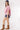 A woman wearing soft pink striped pattern, relaxed boxy silhouette and easy half sleevesshirt, paired with blue denim shorts, brown cowboy boots, and a navy blue baseball cap with a -FleaStyle