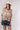 A woman wearing an ivory cowboy hat and a long-sleeve, balloon-silhouette blouse with a colorful paisley and floral print, paired with dark denim shorts-Button Down Paisley Printed Blouse - Pink/Orange