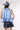 A woman wearing a light blue sleeveless ruffled top, dark blue paisley patterned denim shorts,a dusty blue cowboy hat-Halter Neck Sleeveless Tie Ruffle Top - Light Blue