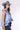 A woman wearing a light blue sleeveless ruffled top, dark blue paisley patterned denim shorts,a dusty blue cowboy hat-Halter Neck Sleeveless Tie Ruffle Top - Light Blue