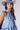A woman wearing a light blue sleeveless ruffled top, dark blue paisley patterned denim shorts,a dusty blue cowboy hat-Halter Neck Sleeveless Tie Ruffle Top - Light Blue