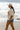 A woman stands on a beach wearing a ivory graphic tee featuring a relaxed fit with bold California orange poppies, denim shorts, and a beige baseball cap, with ocean waves and rocky shoreline in the background--California_Poppy_Oversized_Graphic_T-Shirt_-_Ivory_Orange-Fleastyle.