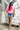 A woman walking down white outdoor stairs wearing a bright pink graphic t-shirt with red flowers, denim shorts, a black baseball cap with 'CALI' in white, and carrying a woven straw bag_ California Poppy Oversized Graphic T-Shirt - Pink/Red_Fleastyle