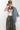A woman wearing olive green camouflage wide-leg pants, a light blue denim jacket draped over her shoulder, a green baseball cap with a butterfly patch, and layered beaded necklaces-Vintage Wooden Beaded Necklace - Pink/Purple-FleaStyle