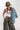 A woman wearing olive green camouflage wide-leg pants, a light blue denim jacket draped over her shoulder, a green baseball cap with a butterfly patch, and layered beaded necklaces-Vintage Wooden Beaded Necklace - Pink/Purple-FleaStyle