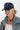 A woman wearing a navy blue trucker hat with a red and blue embroidered butterfly patch, a light-wash denim jacket, a white ribbed tank top, and a patterned camo pants-Butterfly-Patch-Trucker-Hat-Navy-FleaStyle