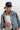 A woman wearing a navy blue trucker hat with a red and blue embroidered butterfly patch, a light-wash denim jacket, a white ribbed tank top, and a patterned camo pants-Butterfly-Patch-Trucker-Hat-Navy-FleaStyle