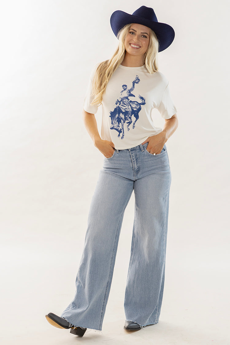 Woman wearing a cowboy graphic white t-shirt  with wide leg blue jeans, blue cowboy hat and cowboy boots-Flea Style