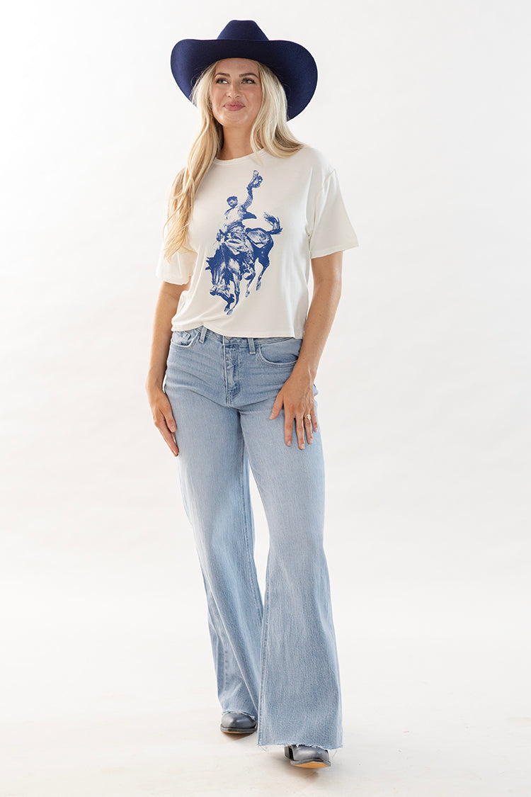 Woman wearing a cowboy graphic t-shirt, light blue wide leg jeans and boots with a navy cowboy hat-Flea Style