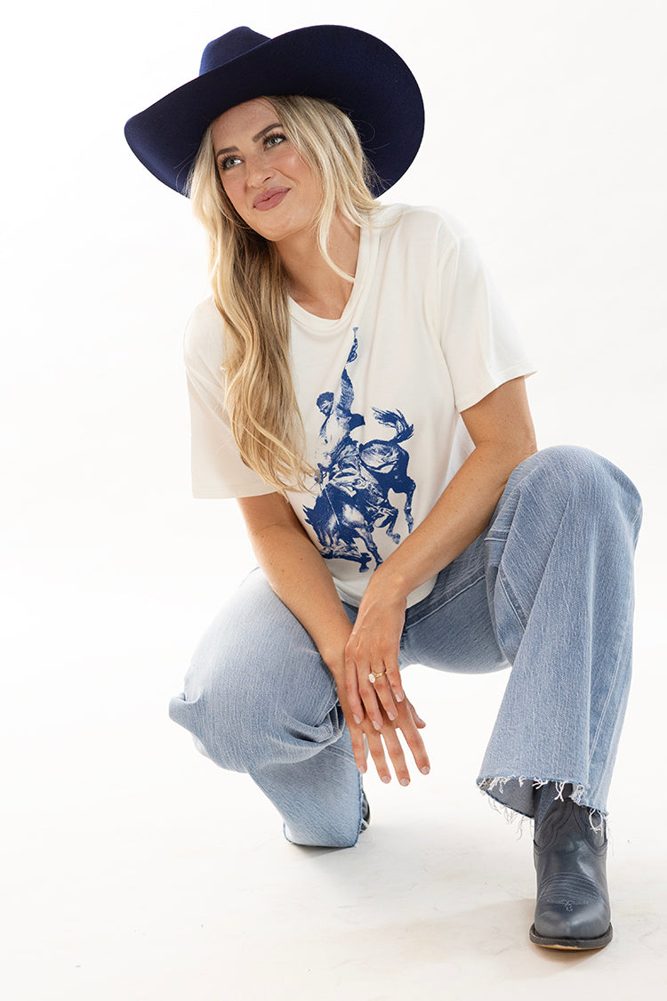 Woman wearing a cowboy graphic t-shirt, light blue wide leg jeans and boots with a navy cowboy hat-Flea Style