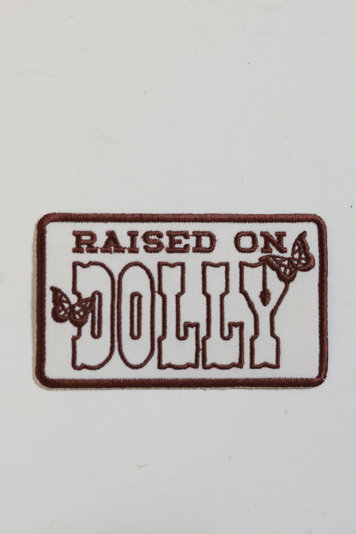 Embroidered  patch with 'Raised on Dolly' brown text and butterfly design. 