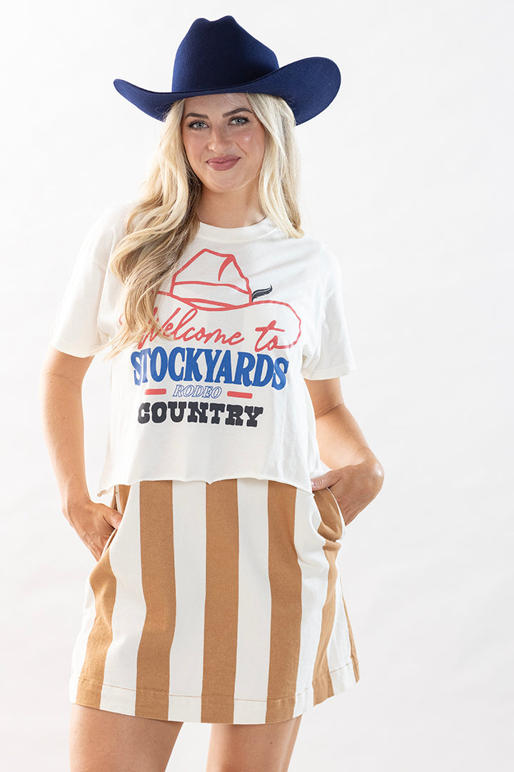 Woman wearing a white cropped graphic t-shirt with vintage rodeo lettering, stripe dress and a blue cowboy hat-Flea Style
