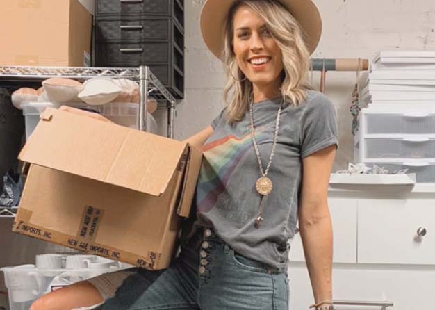 Woman wearing a hat and carrying a card board box 