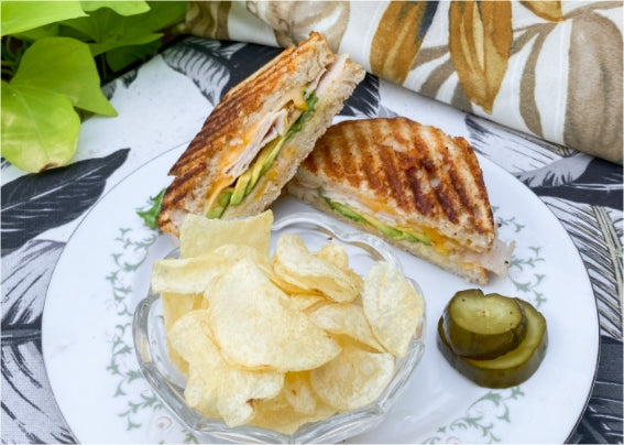 Turkey, cheese and avocado sandwich with chips and pickles